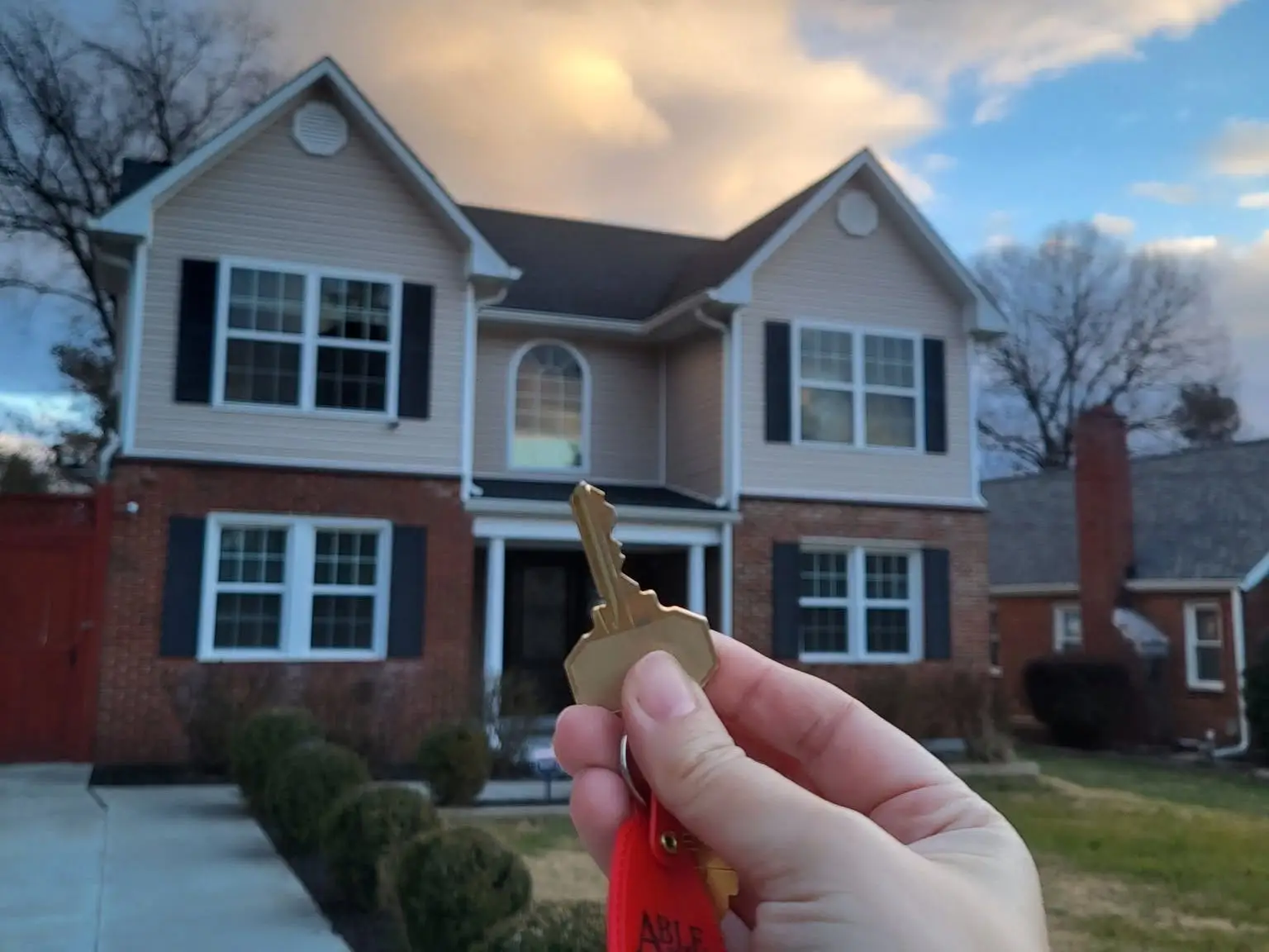 A hand holds a house key in front of the writer's house.