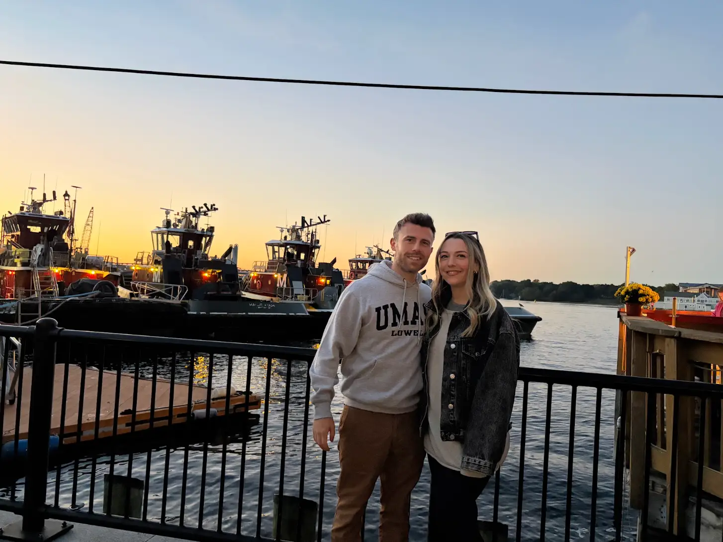 The writer and her husband pose in front of a body of water with boats in the background at sunset.