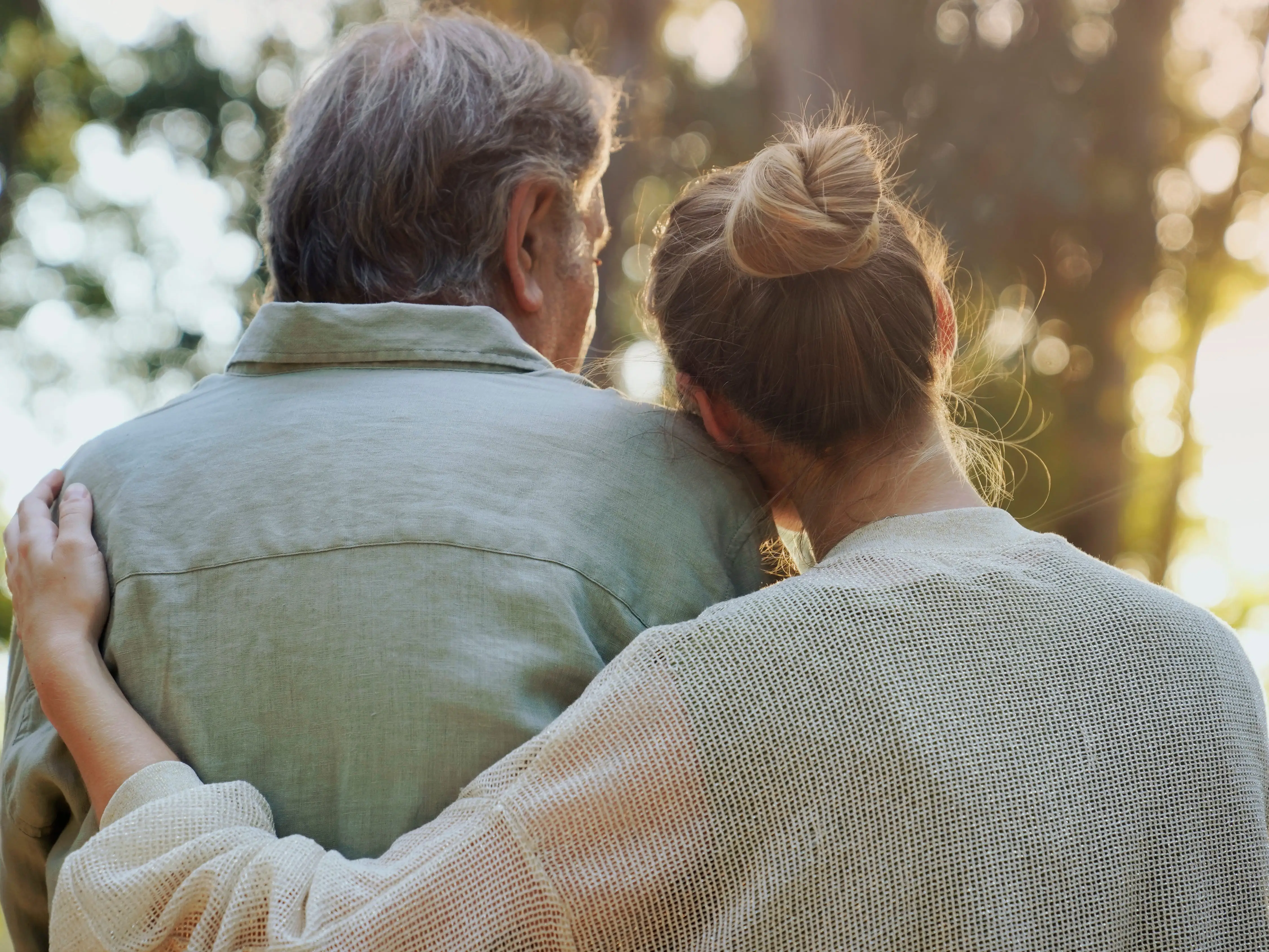 Two people seen from behind embrace outdoors
