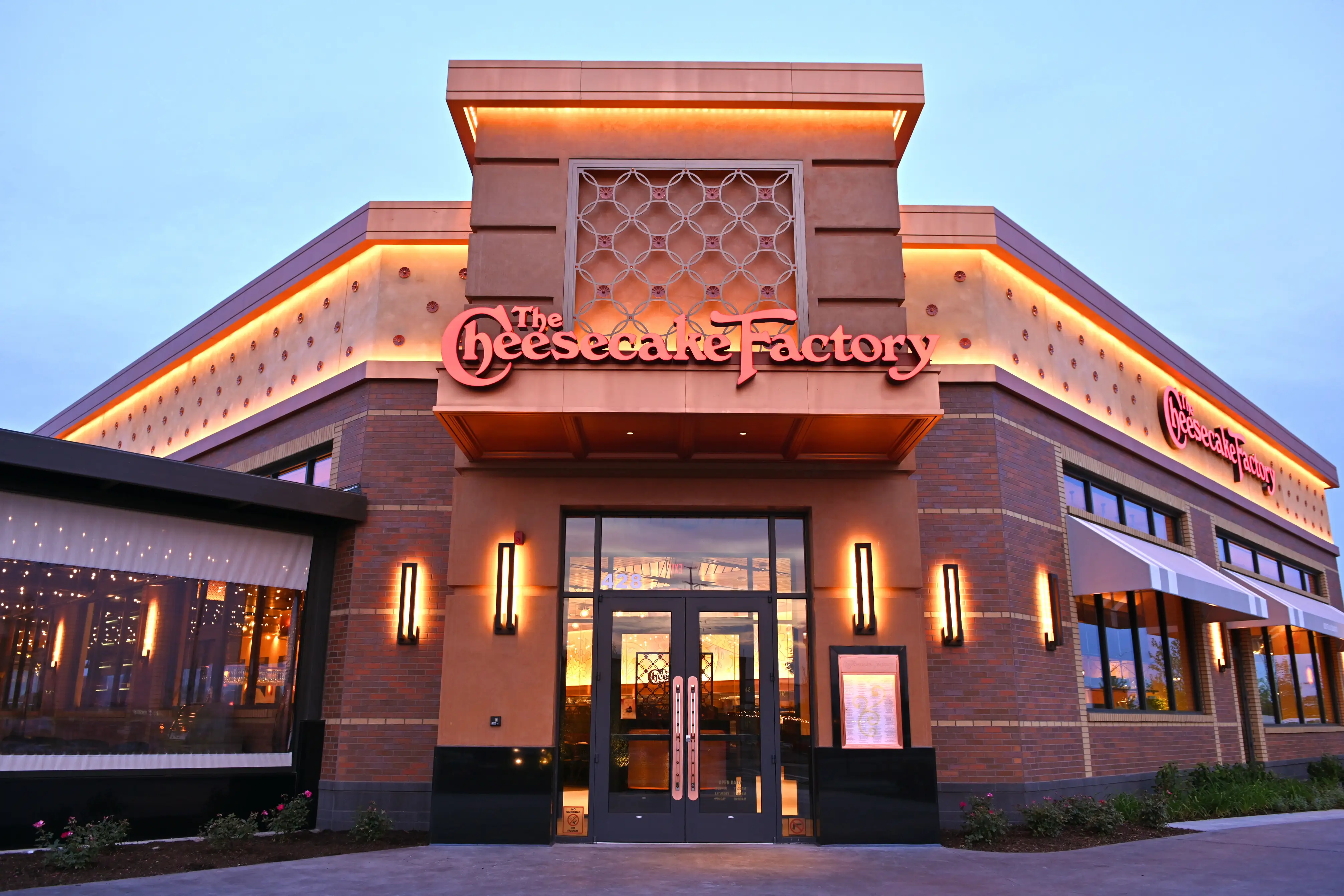 The Cheesecake Factory restaurant exterior with illuminated signage and entrance at dusk.