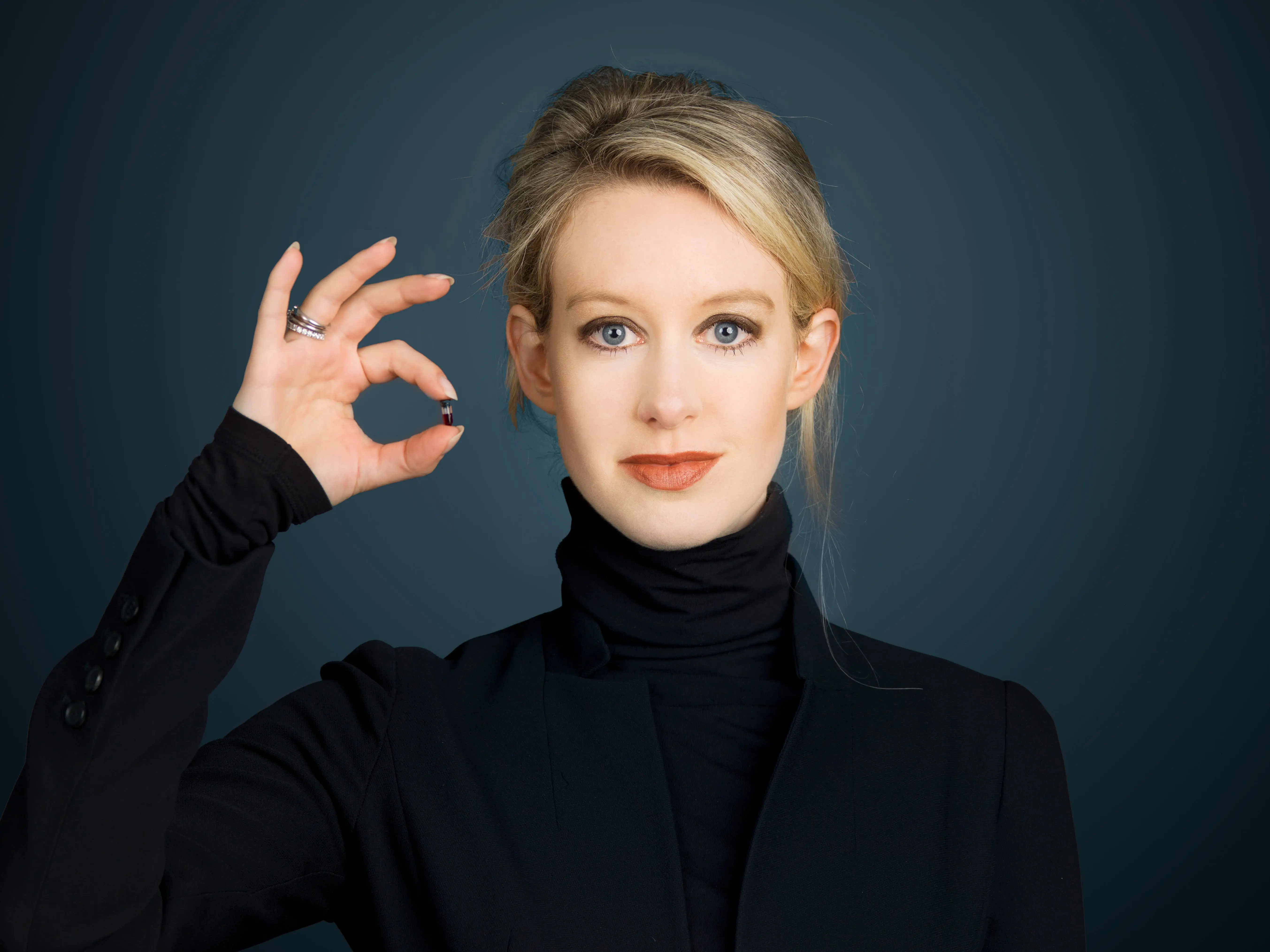 Elizabeth Holmes in a black turtleneck holding a pill.