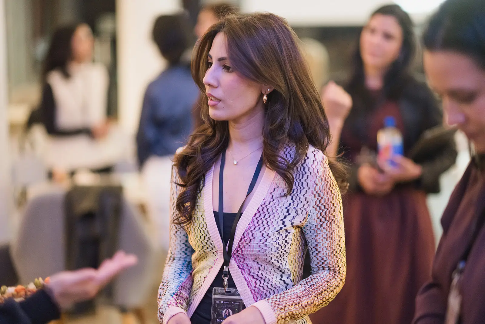 Attendee wearing a lanyard stands among blurred people at an indoor networking or conference event.