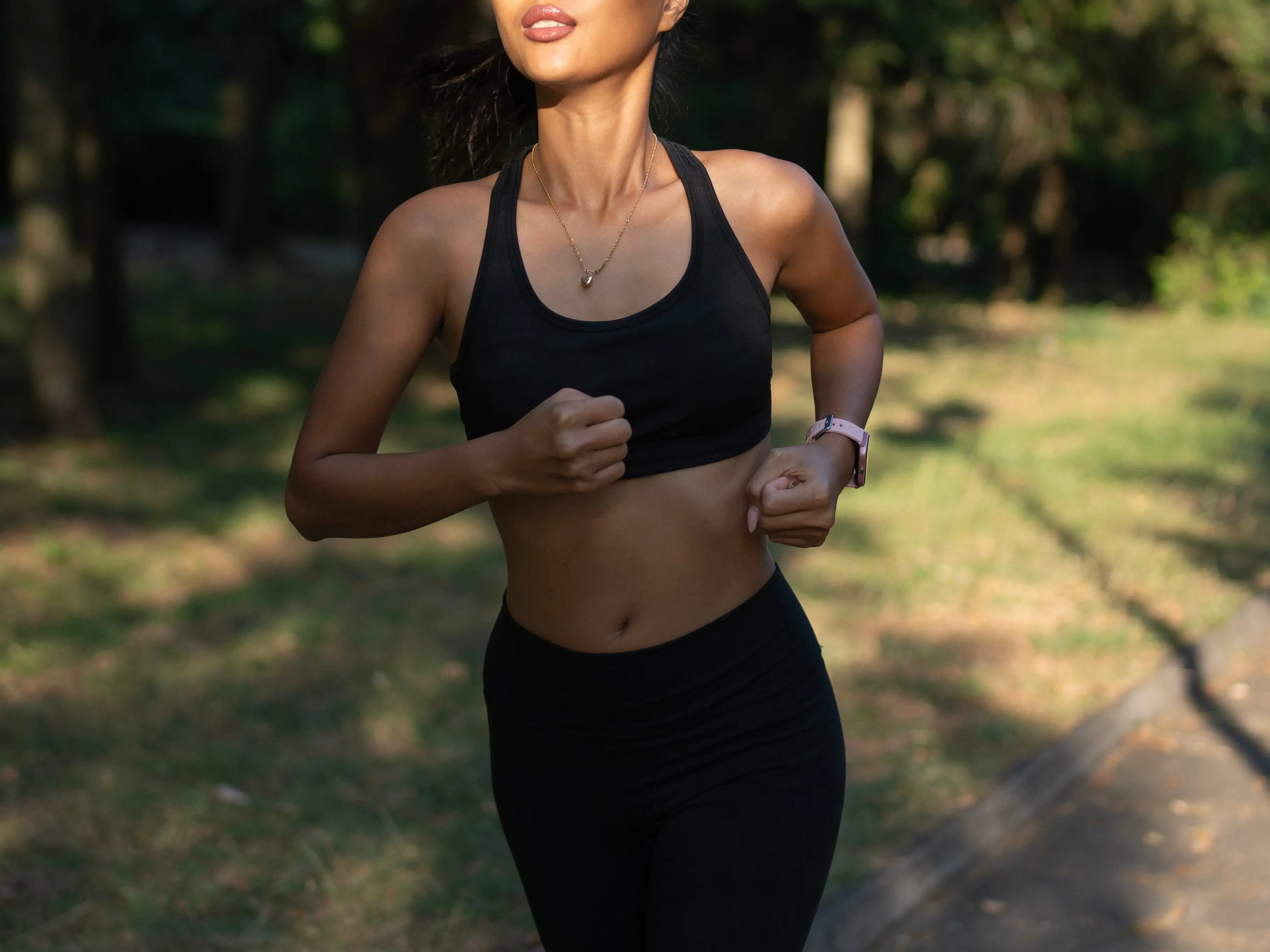 Fit female jogger running outdoors surrounded by greenery.