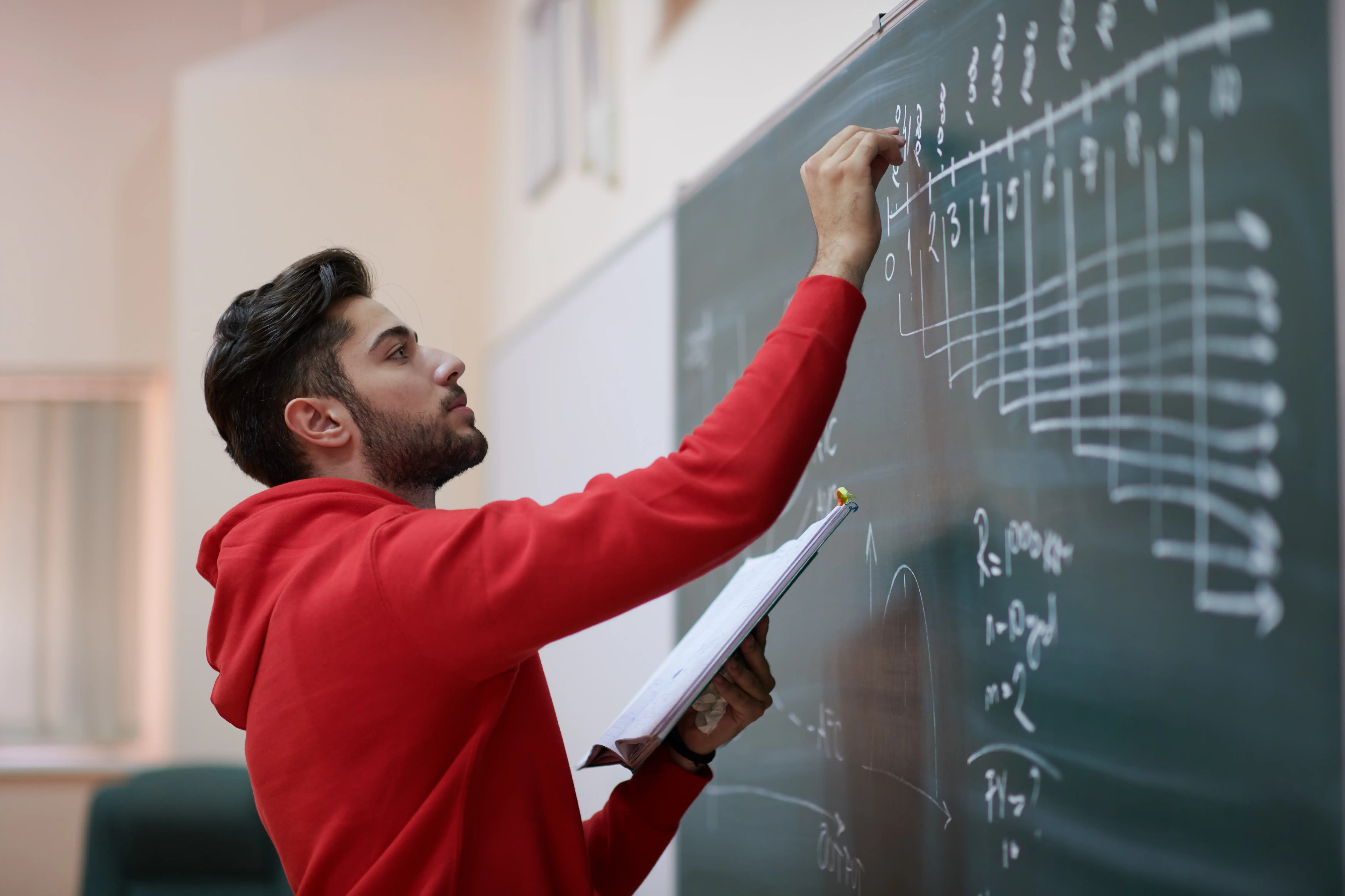 A stock image of a student writing on a chalkboard in a classroom.