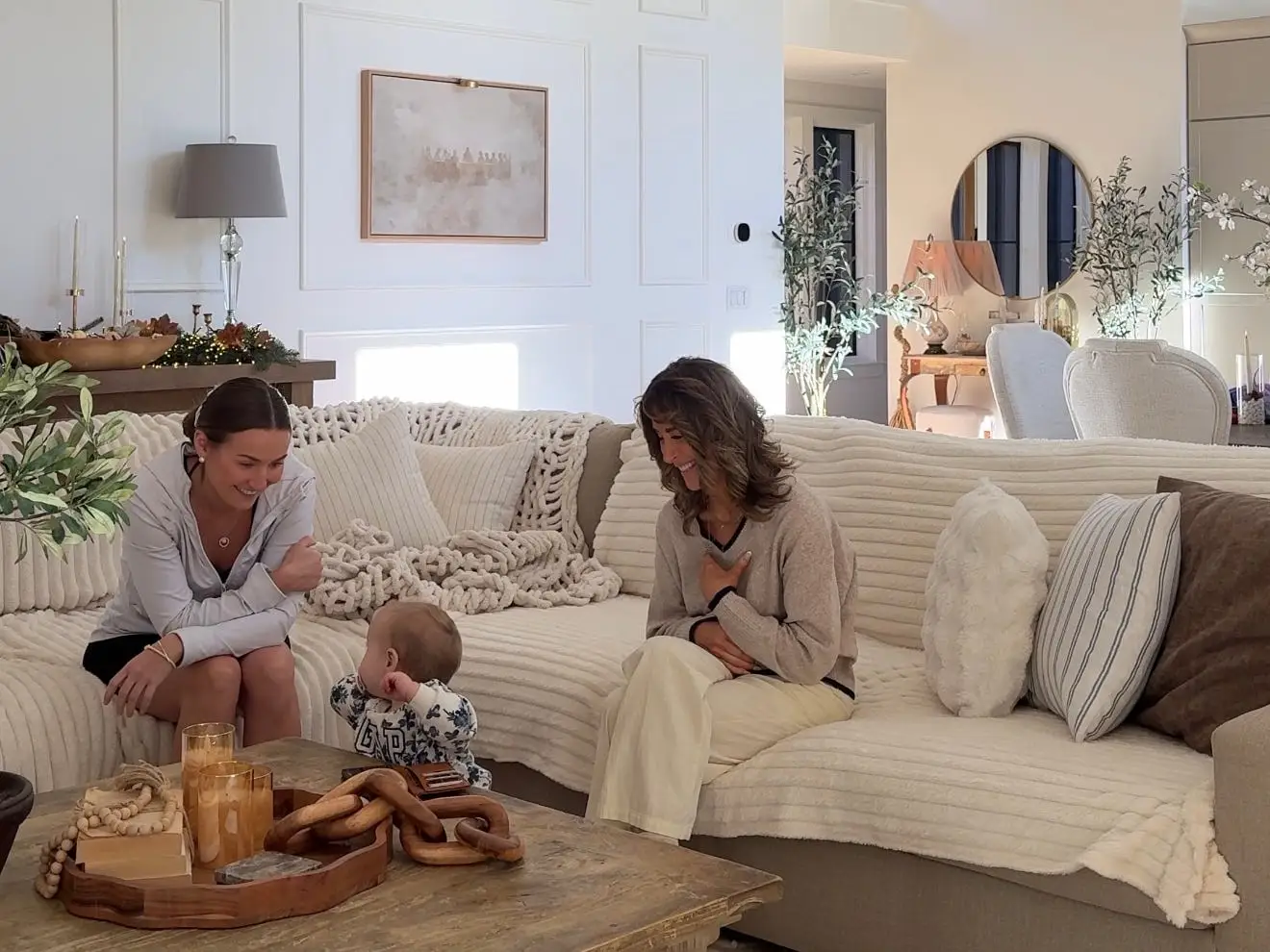 Taylor sits on the couch with her mom. They're both smiling at Taylor's daughter.