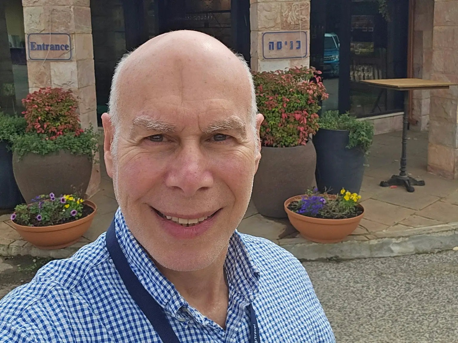 A man in a blue-collar shirt is taking a selfie outside a winery.