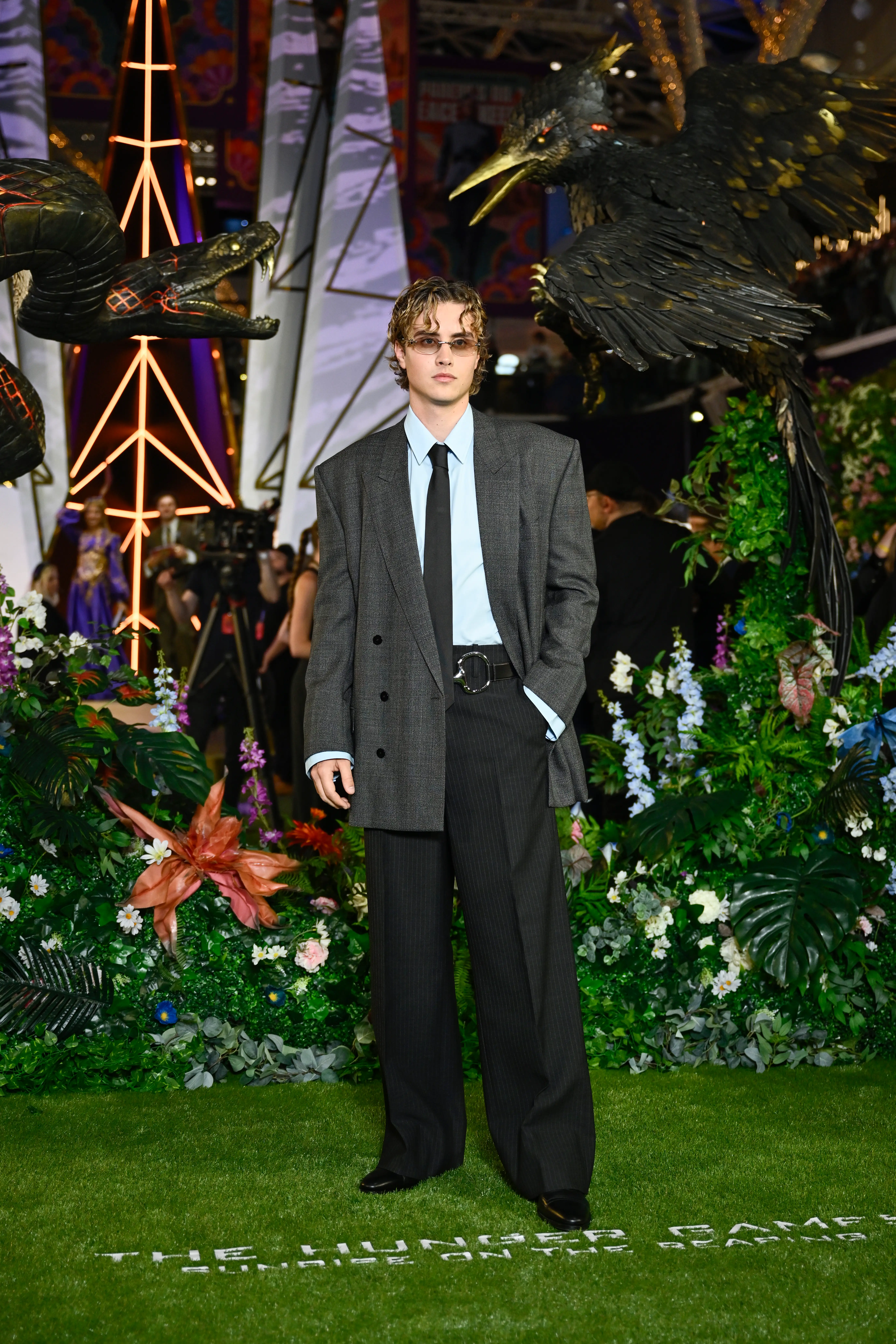 Joseph Zada stands on a green carpet amid tropical plants and large bird sculptures at a themed event.