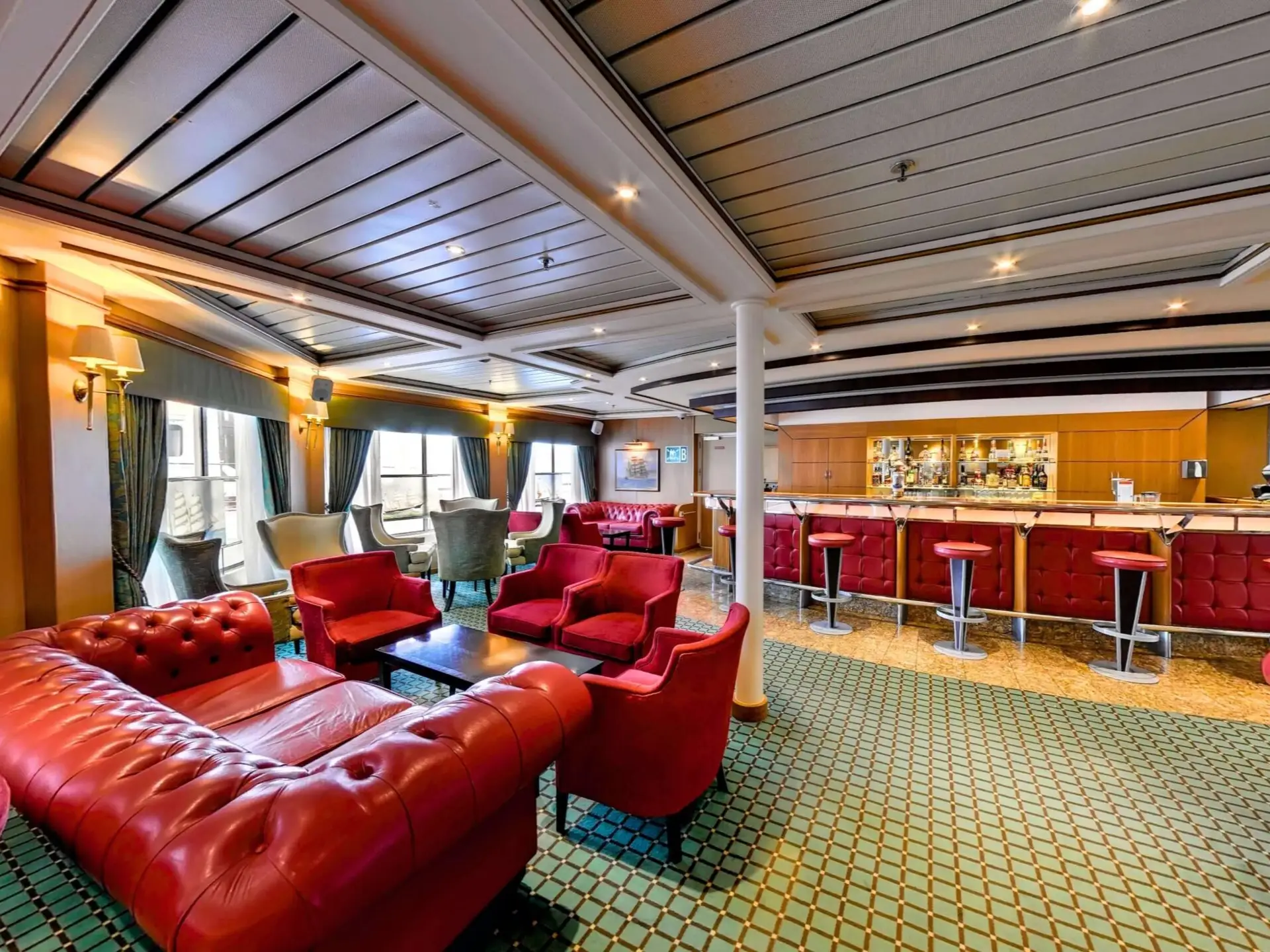 Elegant lounge bar with red leather seating, bar stools, wood paneling, large windows, and patterned green carpet.