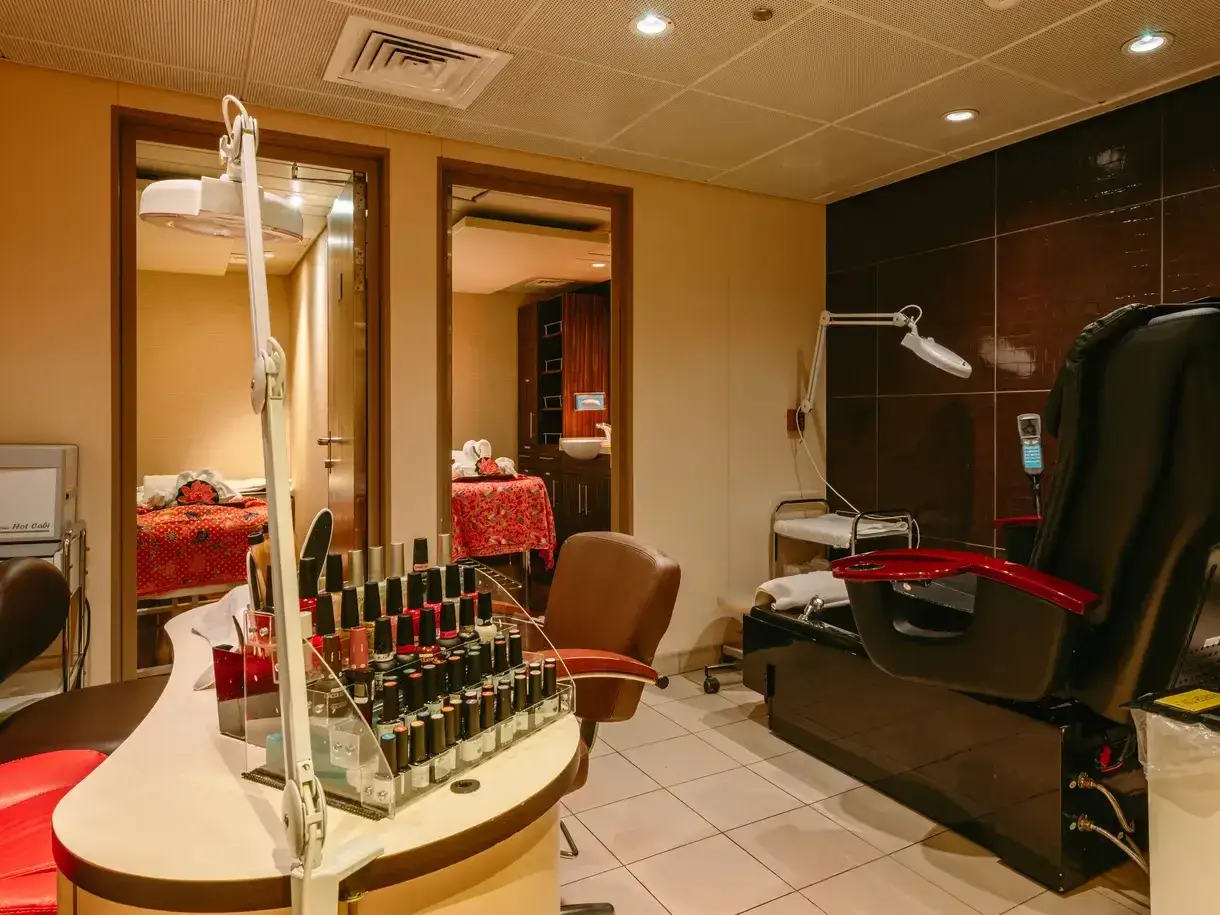 Spa treatment room with manicure polish display, pedicure chair, lamps, and massage tables in adjoining rooms.
