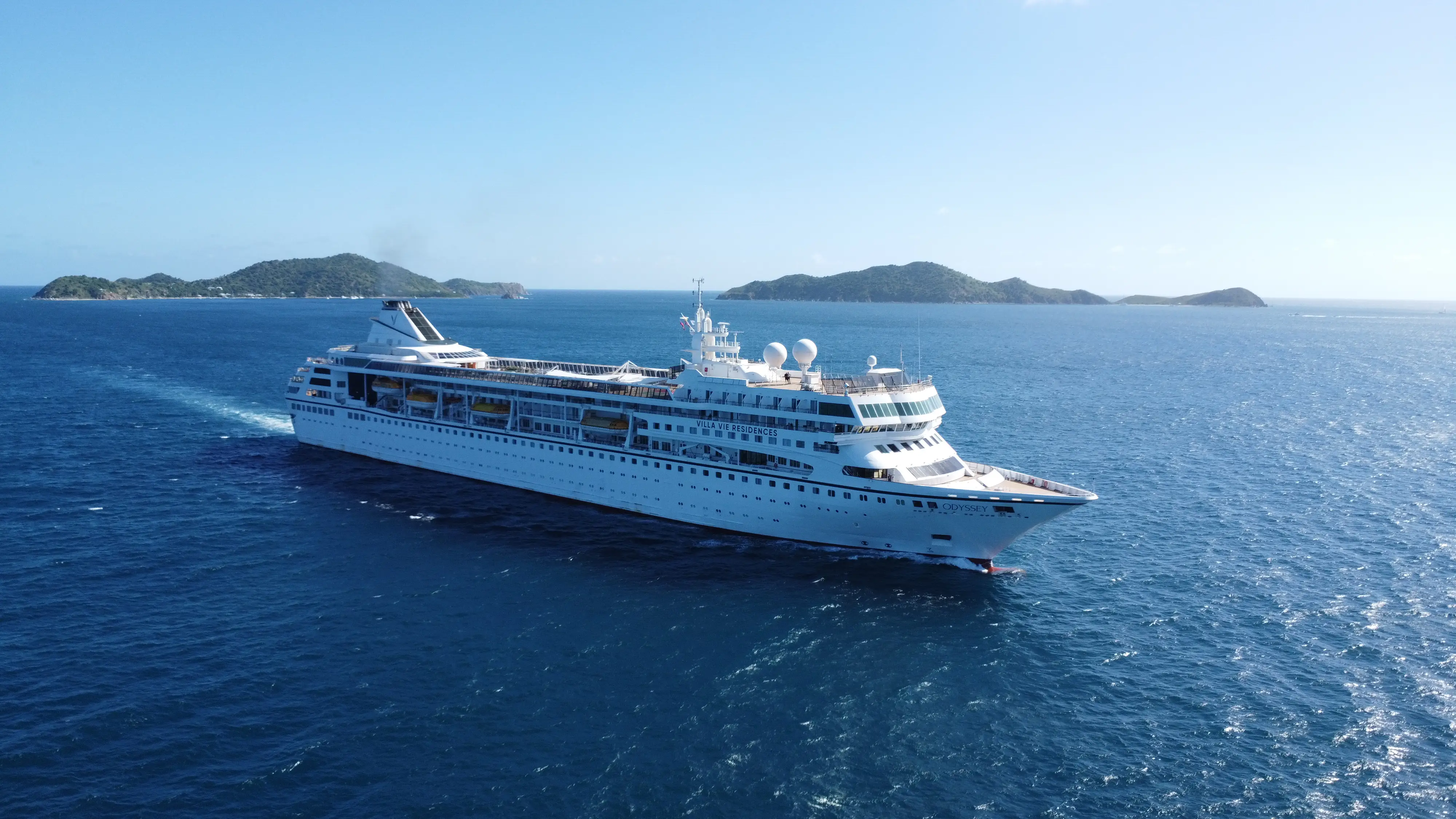 Royal Caribbean cruise ship Jewel of the Seas sails through blue water near green islands.