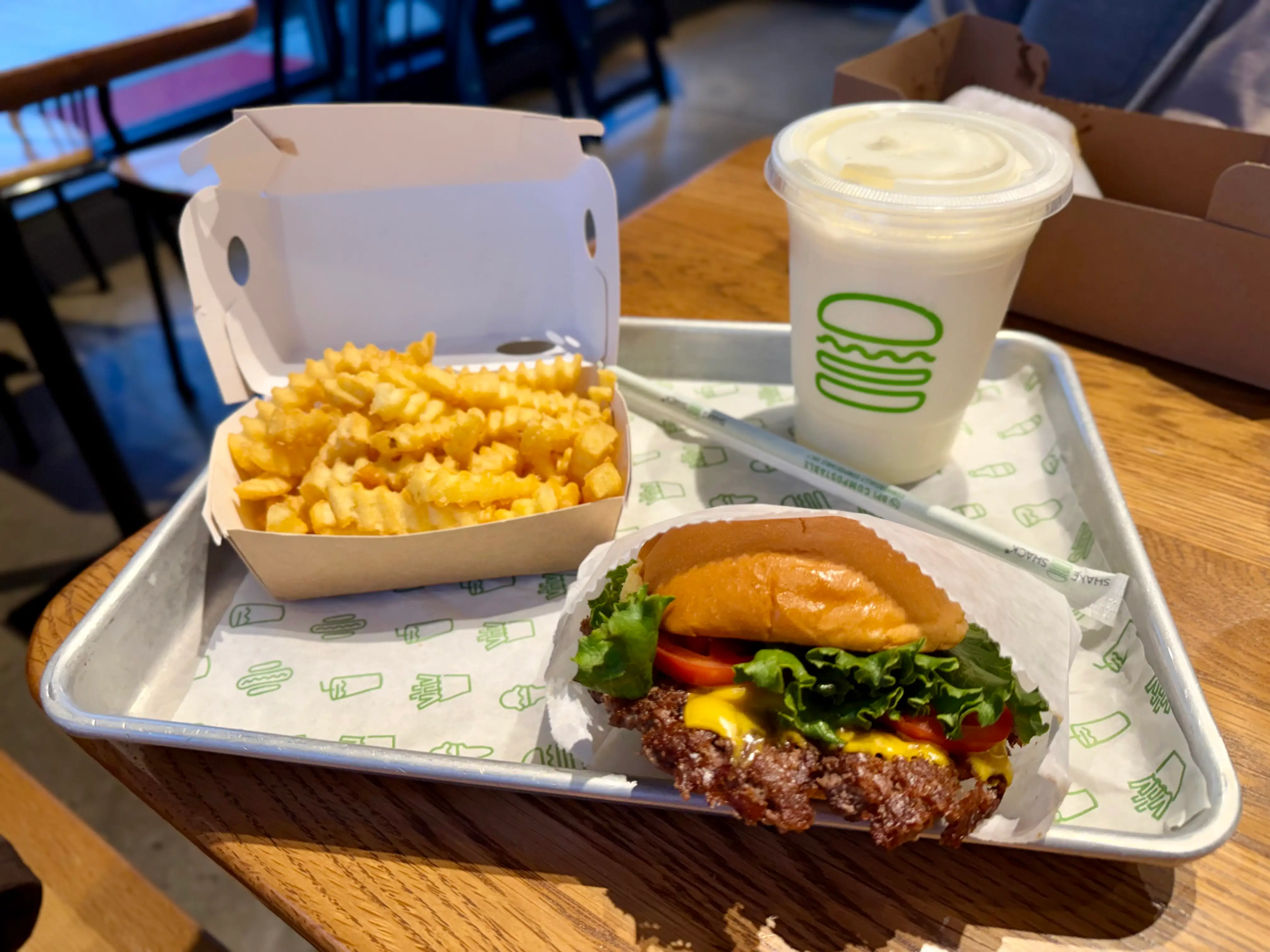 A cheeseburger, a vanilla milkshake, and a container of crinkle-cut fries on a metal tray.