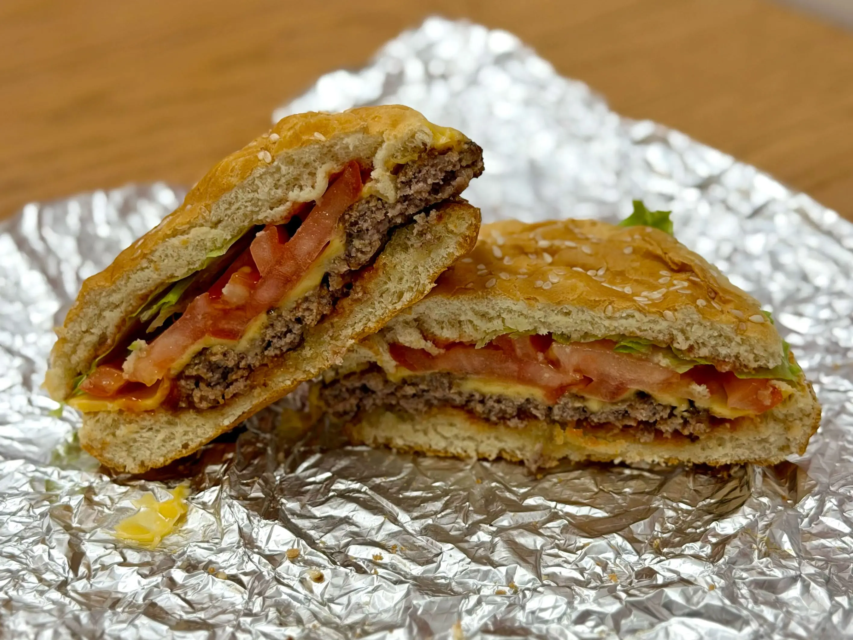 A cheeseburger with lettuce, tomato, and pickles that's been sliced in half.