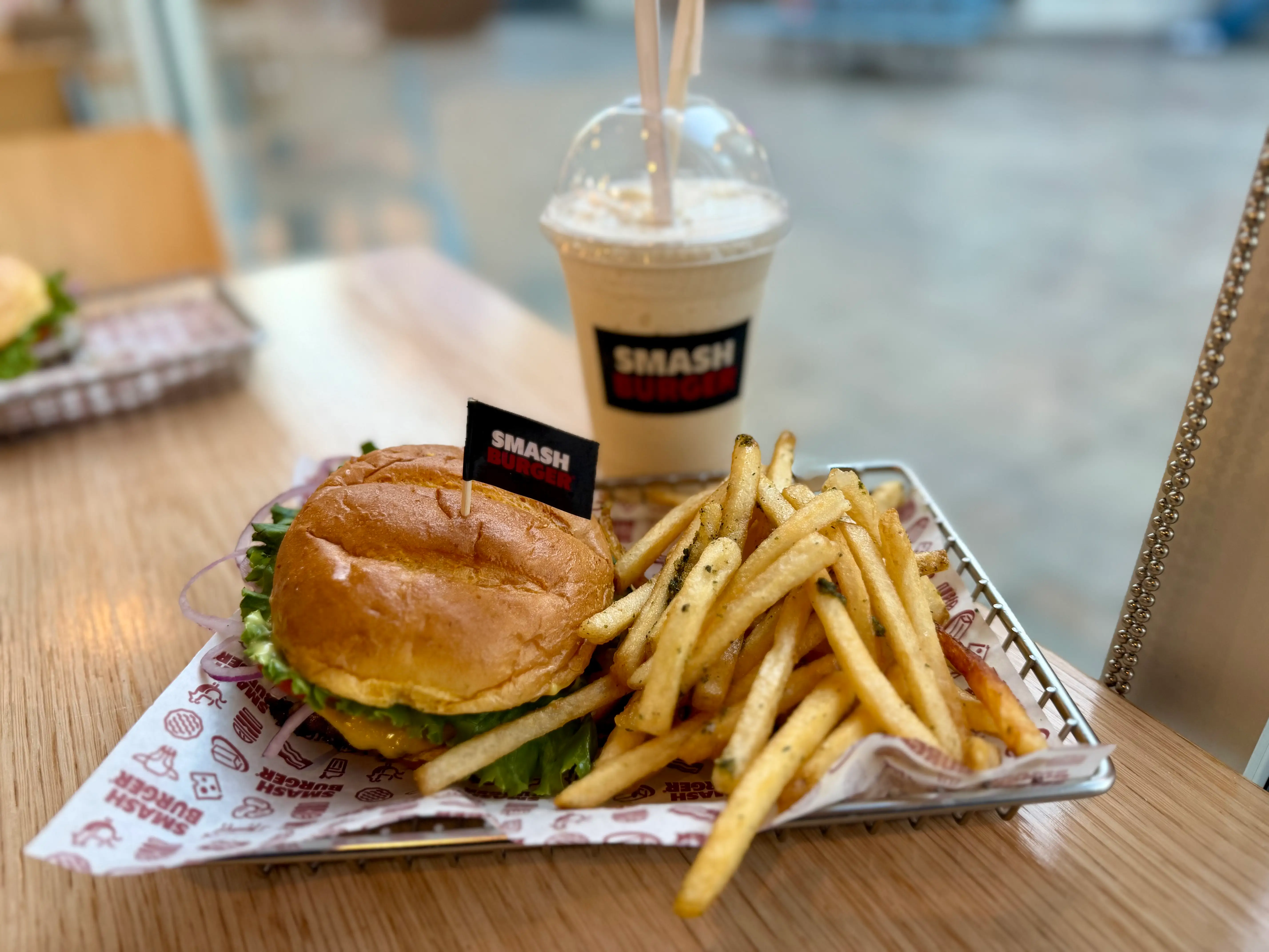 A cheeseburger and fries on a metal tray, with a vanilla milkshake behind it.