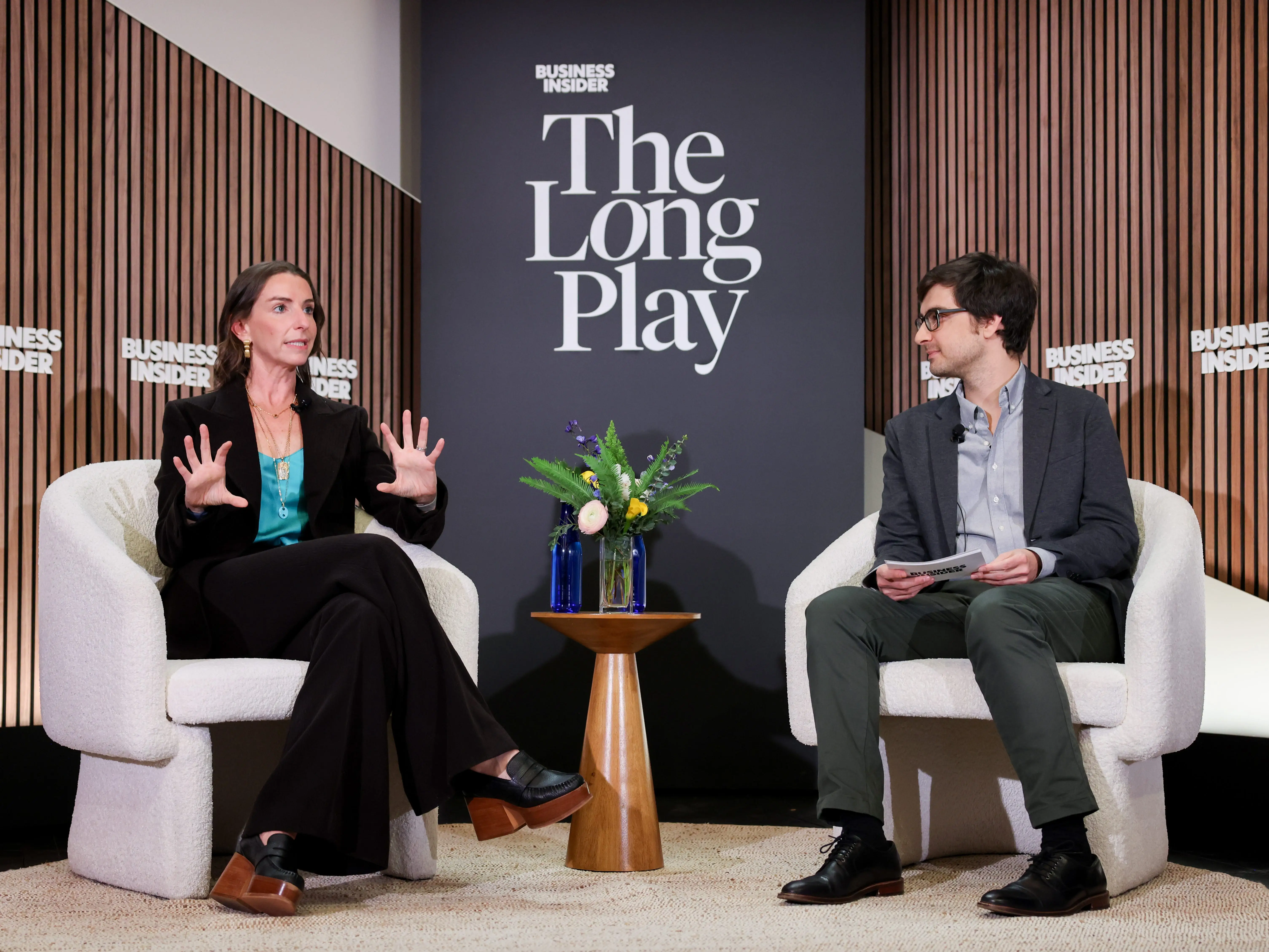 Two speakers sit onstage for a Business Insider The Long Play conversation beside a small table with flowers.