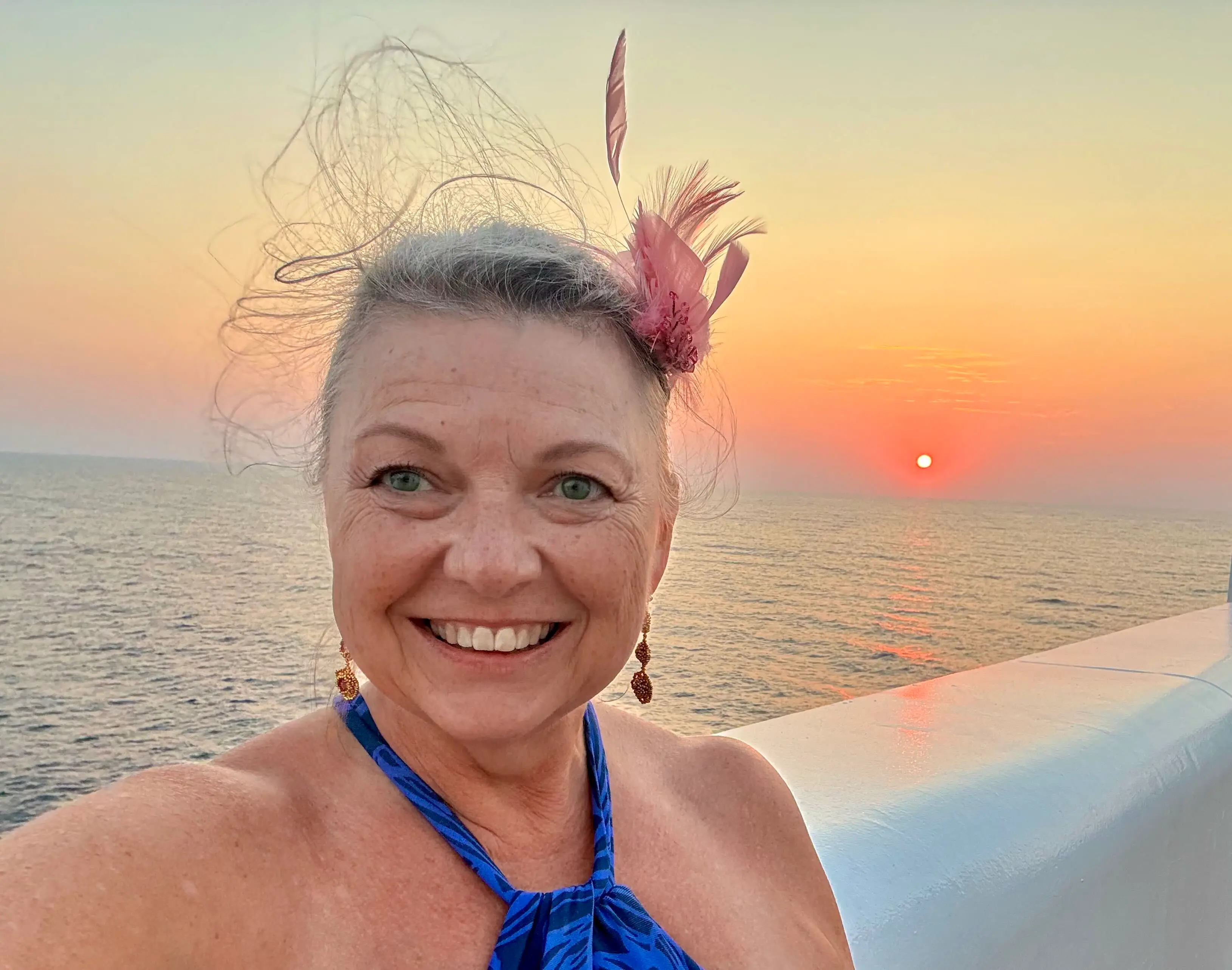 A woman taking a selfie on a ship during sunset.