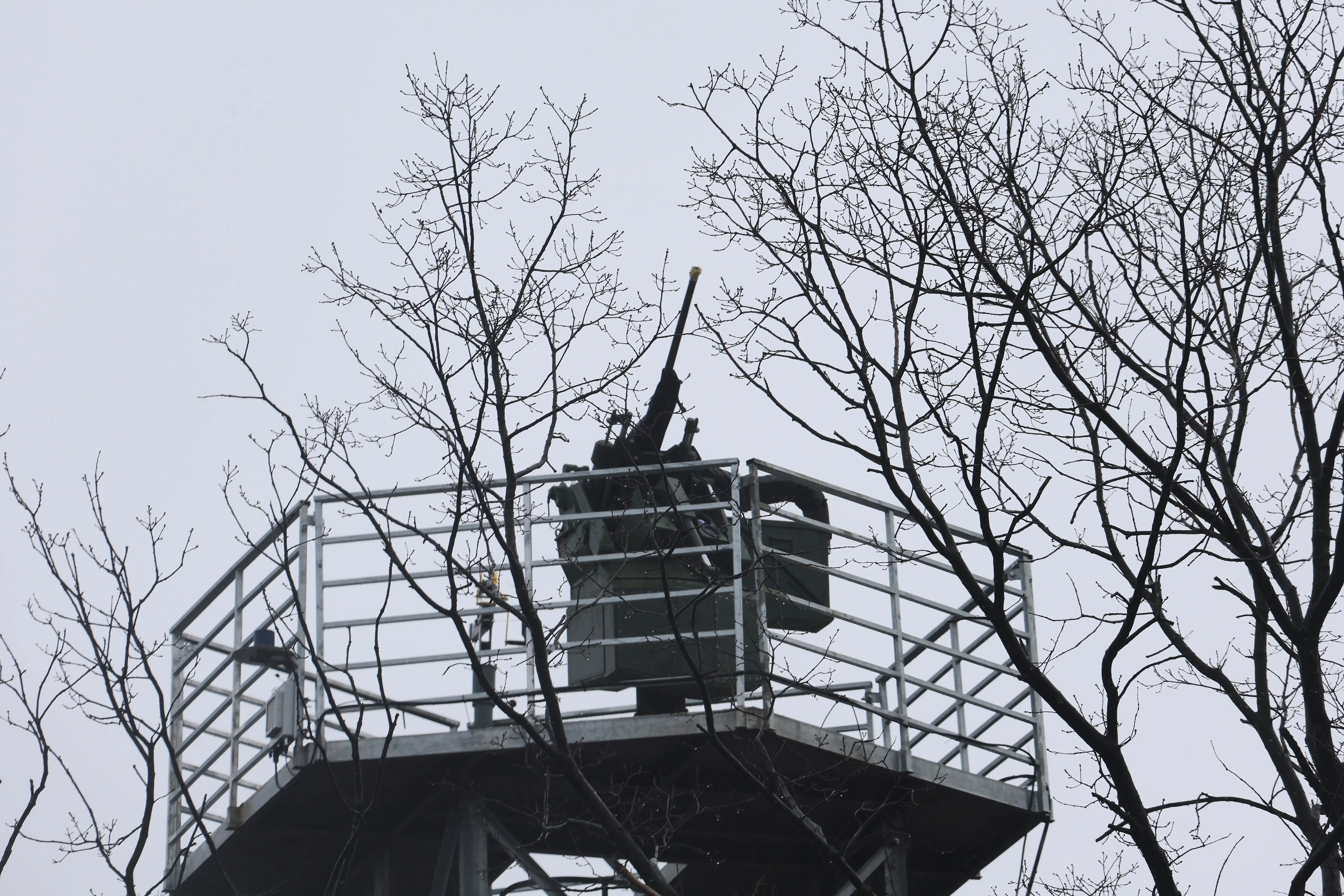 An automatic turret sits on top of a tower above the treeline.