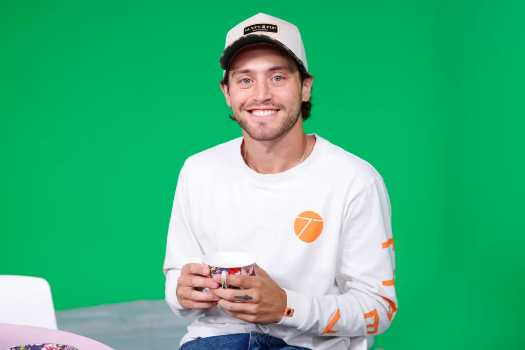 Liam Obergfoll smiling while holding a teacup in front of a green screen.