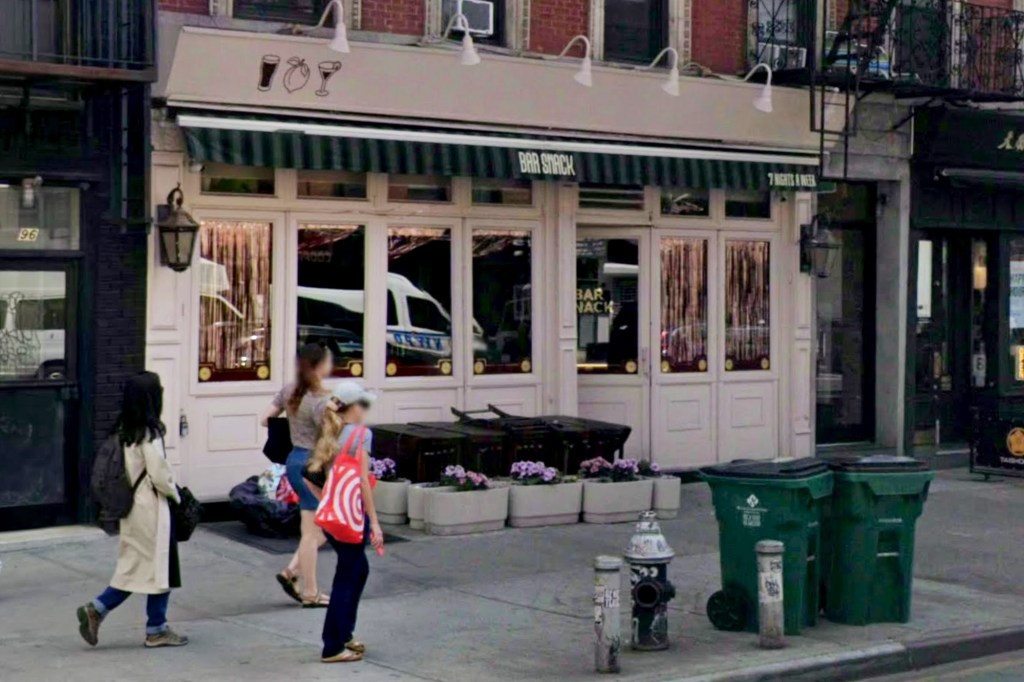 Exterior view of Bar Snack on 2nd Avenue in New York City, featuring a striped green awning, large windows reflecting the street, and pedestrians walking past on the sidewalk.