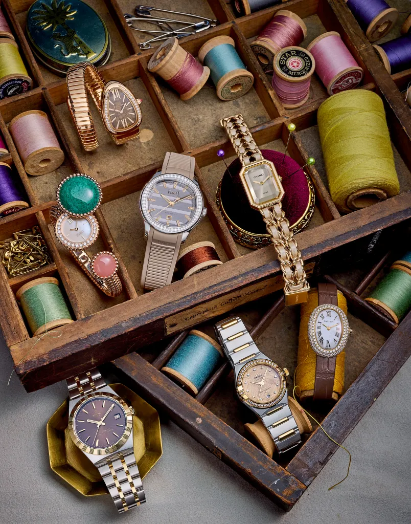 A collection of luxury watches and colorful spools of thread displayed in a wooden compartment box.