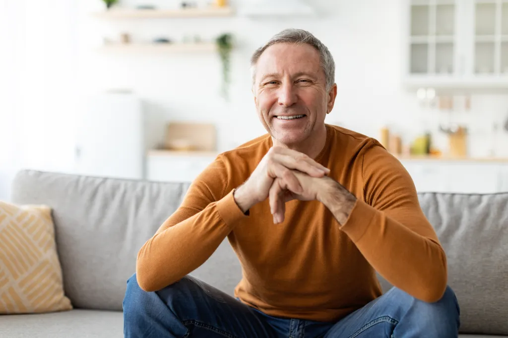 A smiling mature man sitting on the couch and posing