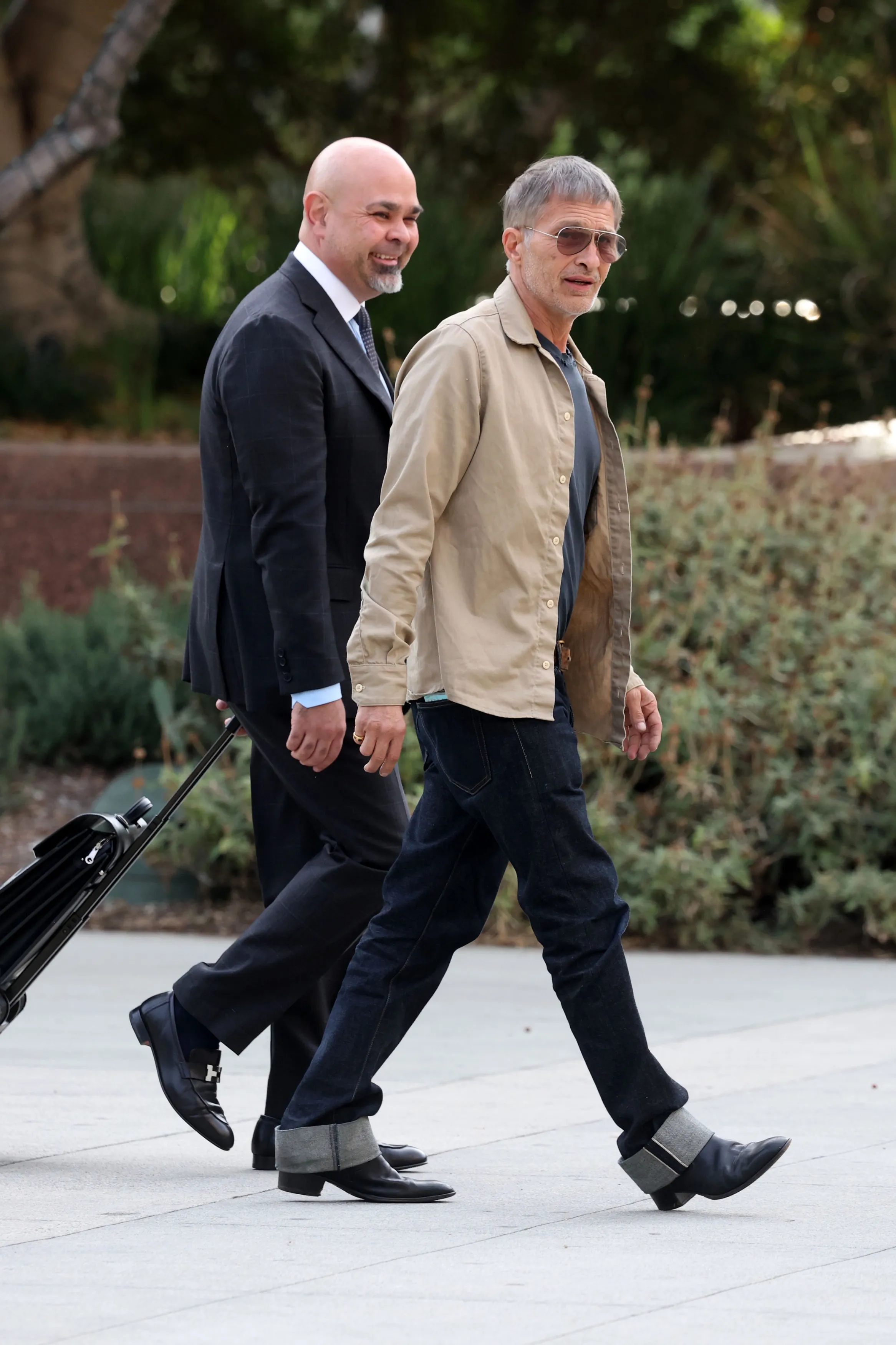 Olivier Martinez walking outside with a man in a suit carrying luggage.