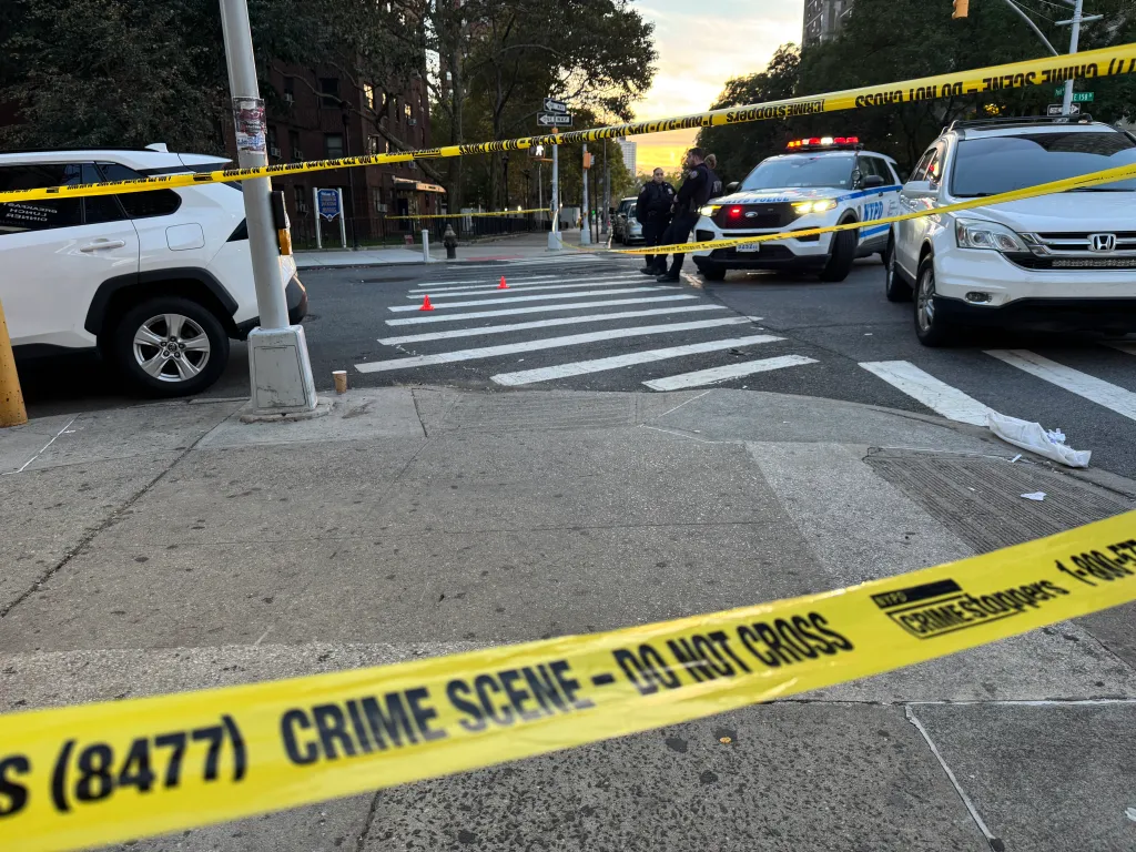 Yellow police crime scene tape blocks off a city intersection with police cars and officers present.