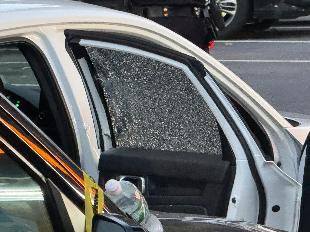 A shattered side window of a white vehicle, with a water bottle resting near the door.