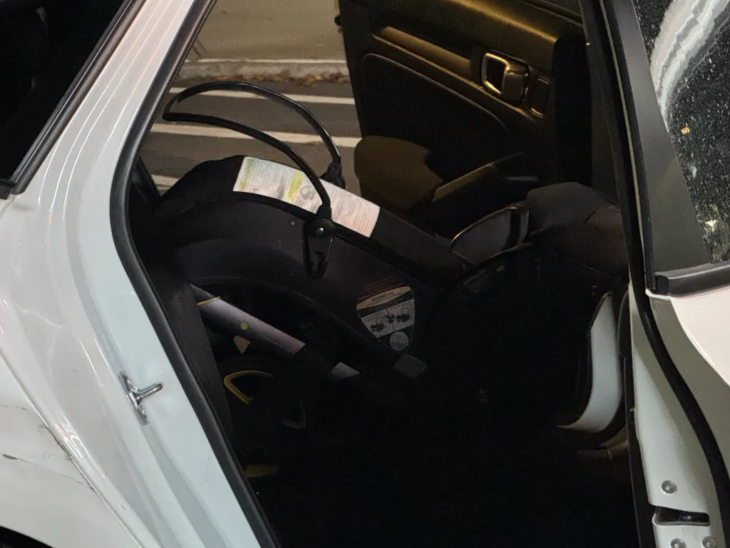 An infant car seat is installed in the back seat of a white car.