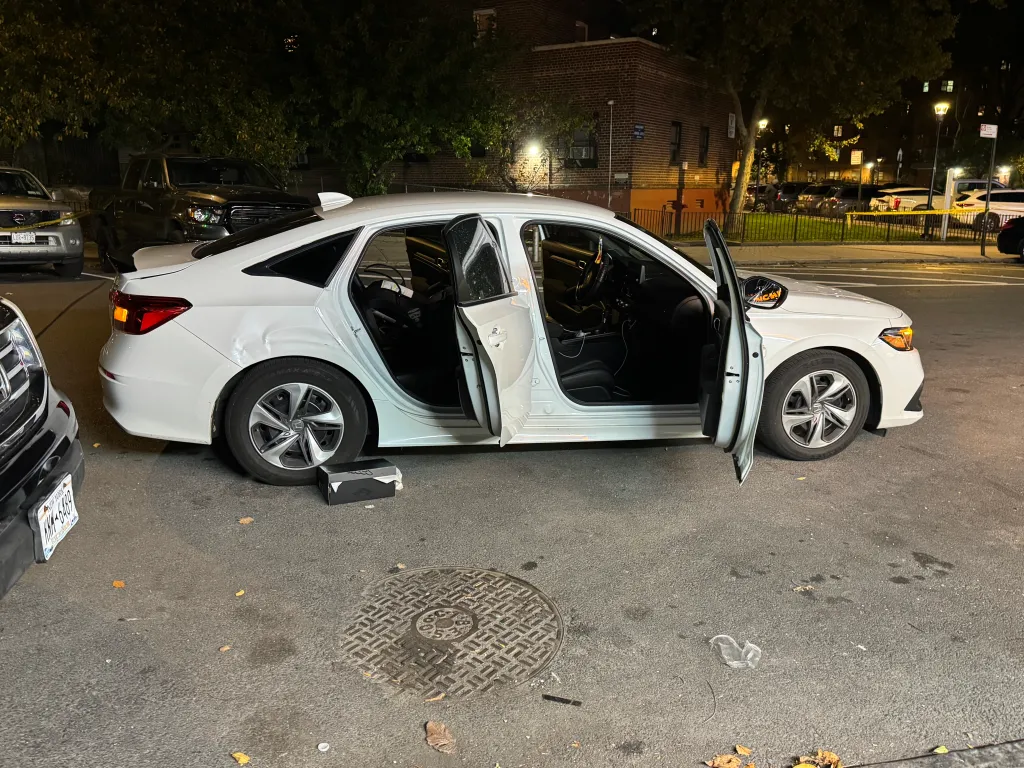 A white sedan parked on a street at night with its doors open.