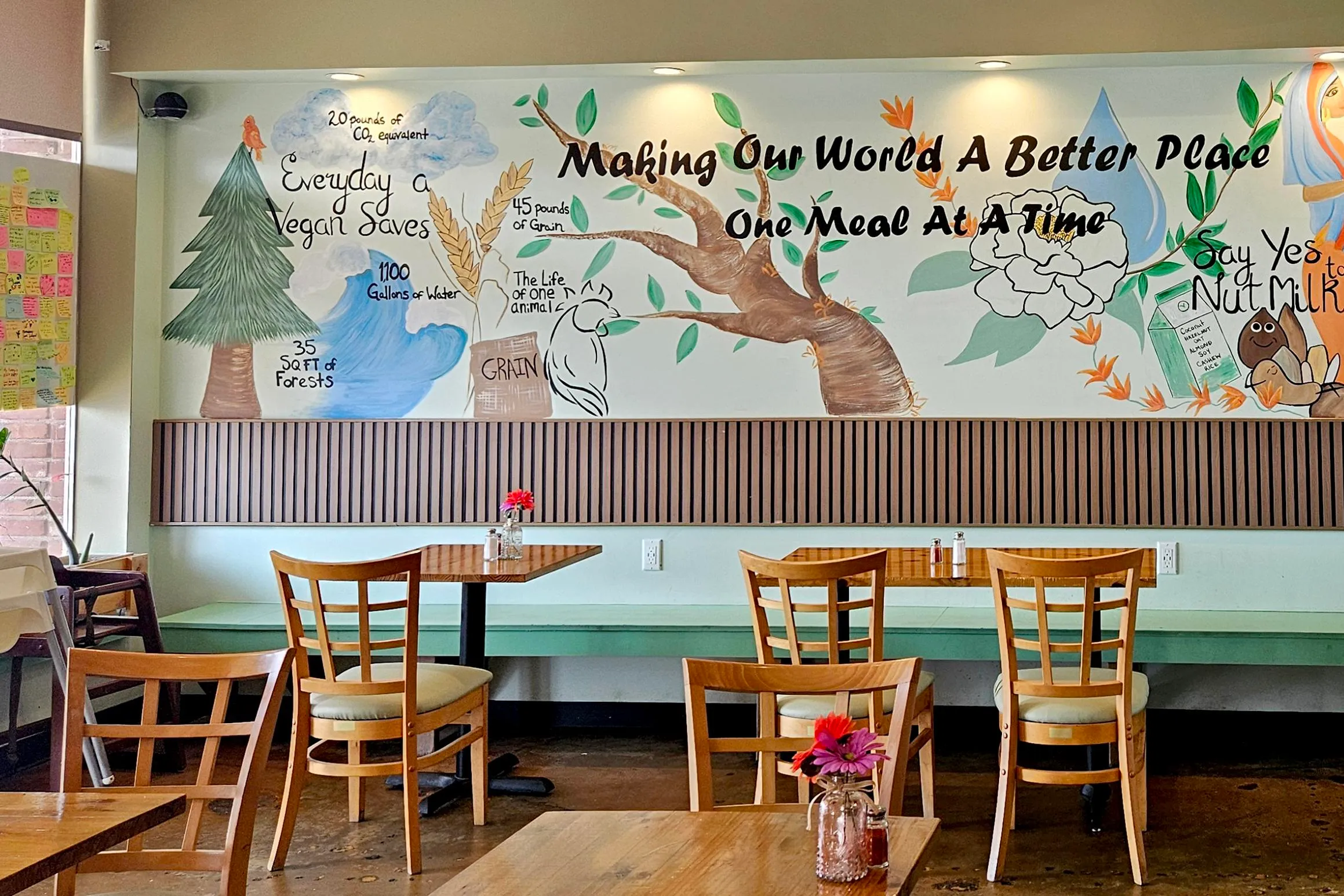 a painted mural on the wall of a cafe reads “Making our world a better place one meal at a time” and depicts various natural elements and food items.