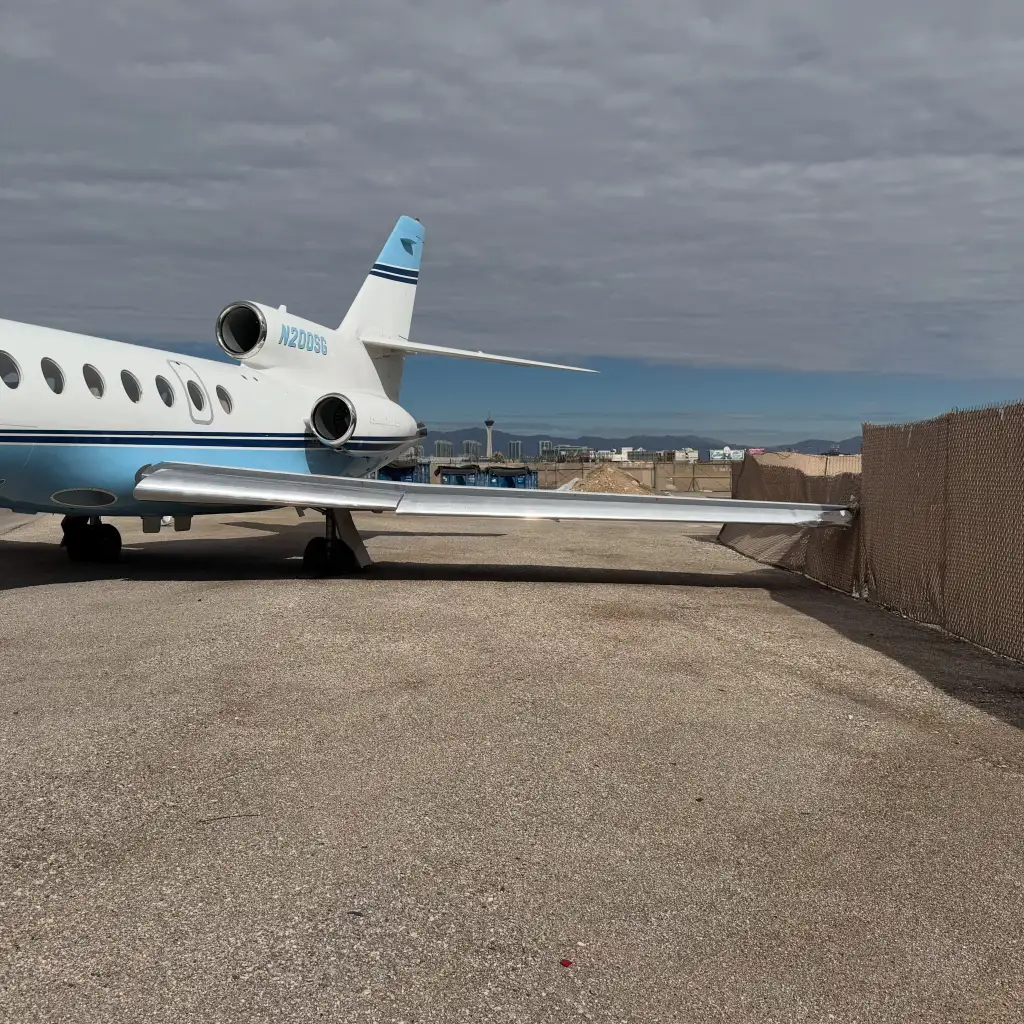 An airplane with its wing pushed through a chain-link fence.