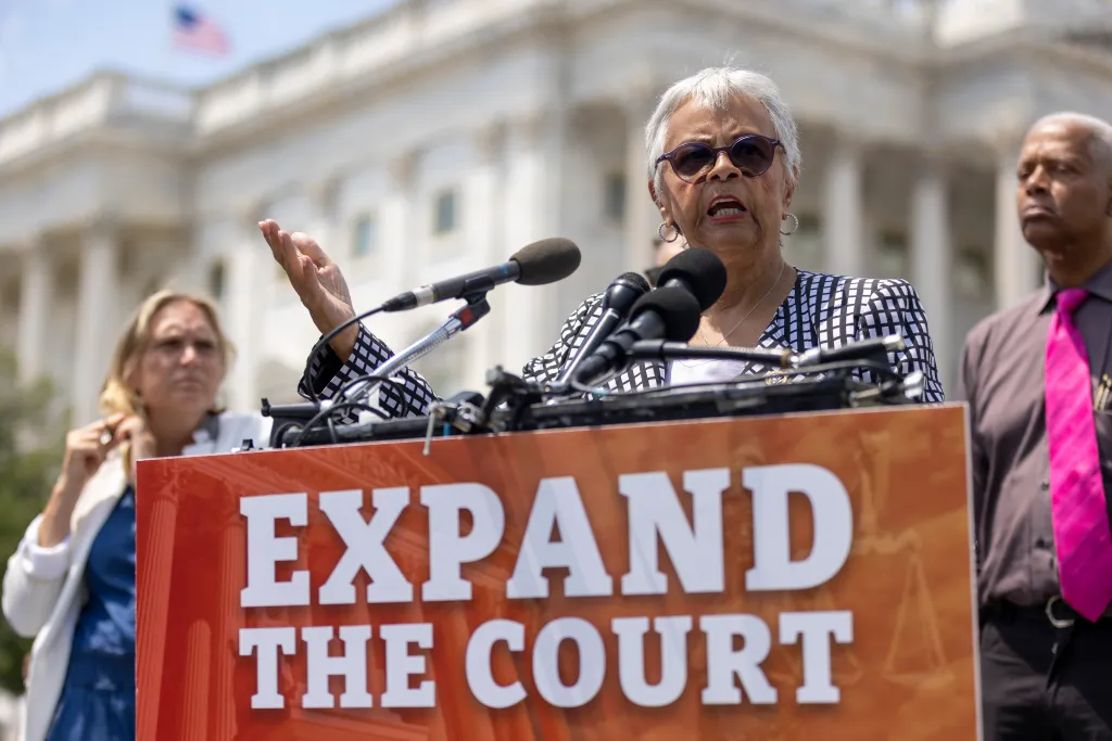 Representative Hank Johnson and other speakers stand at a press conference in front of the US Capitol, with a sign reading