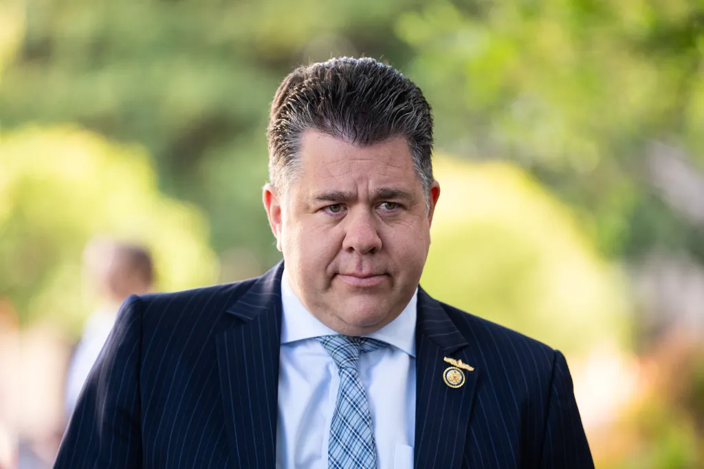 Close-up photo of Matt Gaetz wearing a dark pinstripe suit and a light blue patterned tie outdoors.