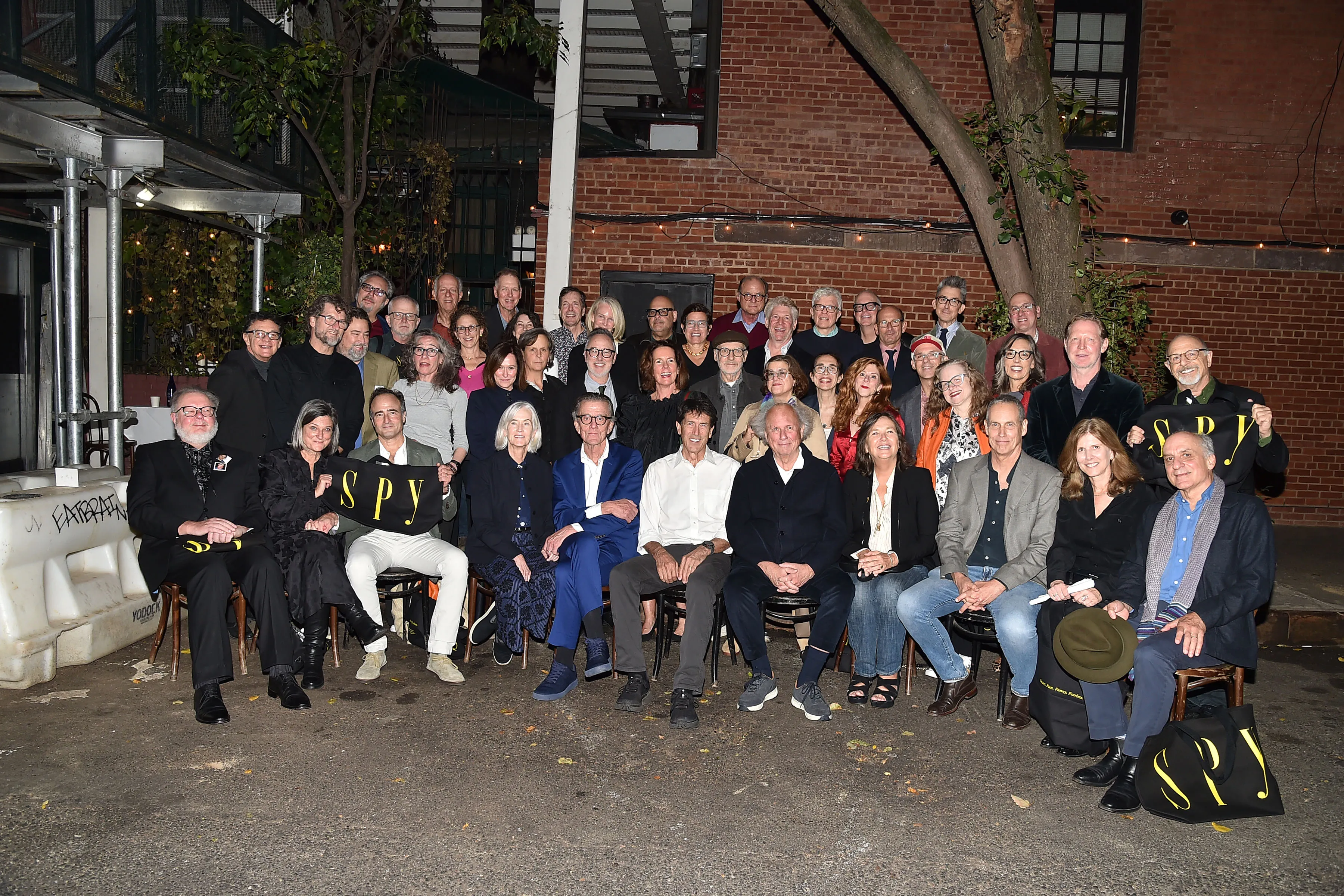 A large group of people posing for a photo outdoors at night, with some holding black bags with the word 
