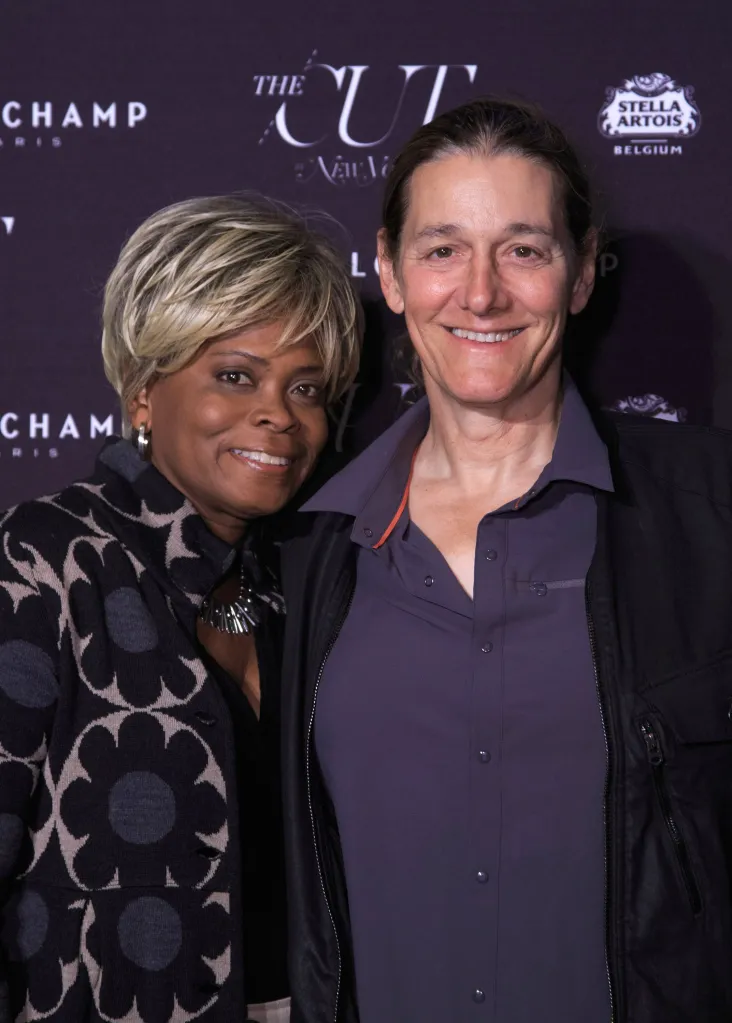 Two women smiling together in front of a dark backdrop with brand logos.