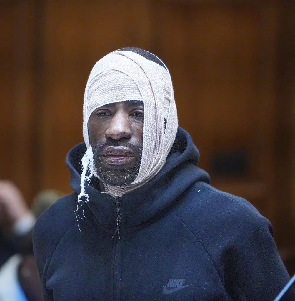 A man wearing a black hoodie with his head wrapped tightly in medical gauze.