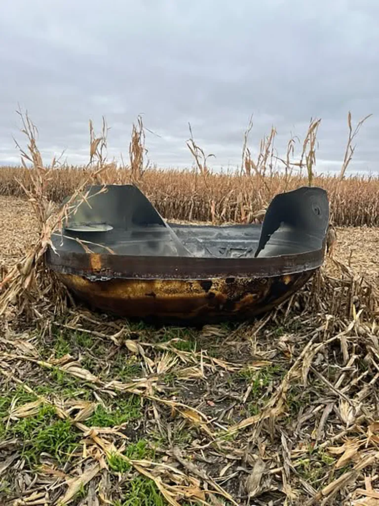 A piece of scorched metal debris, suspected to be from a space capsule, sits in a harvested cornfield under an overcast sky.
