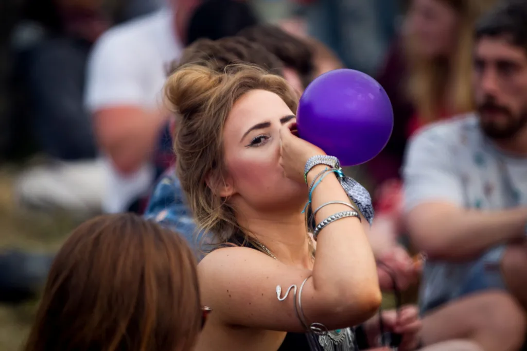 A woman inhaling from a balloon at a music festival.