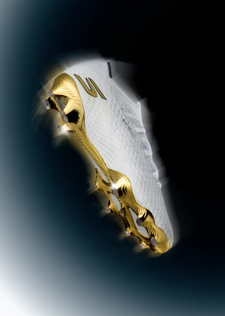 A white and gold soccer boot against a dark background with motion blur effects.
