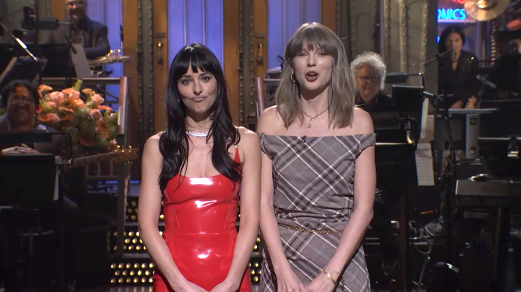 Dakota Johnson and Taylor Swift stand side-by-side on the SNL stage with the band in the background.