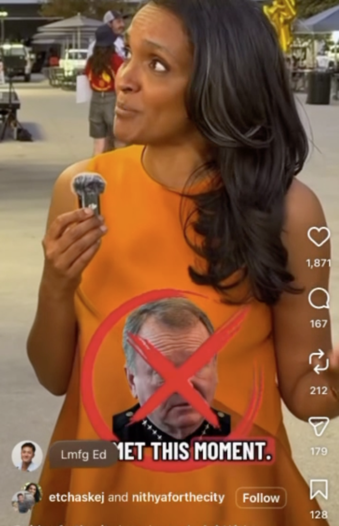 A woman wearing an orange dress and holding a small microphone, with a superimposed graphic of a man's face crossed out over her chest.