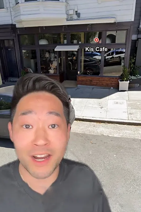 A man standing in front of Kis Cafe, with a digital map pin overlaying the storefront.