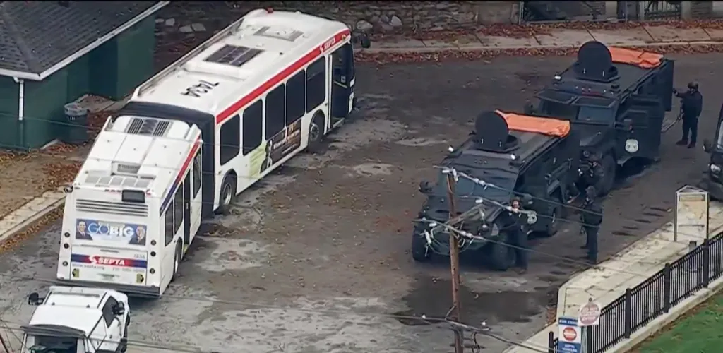 An aerial view shows a SEPTA bus parked next to two black armored police vehicles with several officers standing nearby.
