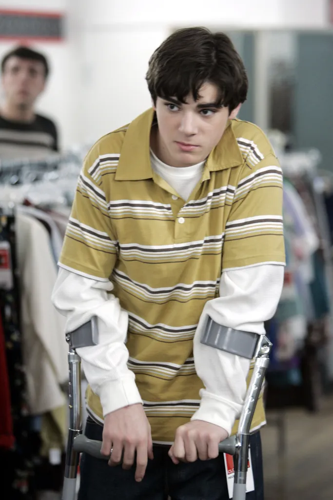 A young man leans on forearm crutches inside a clothing store, looking thoughtfully to the side.