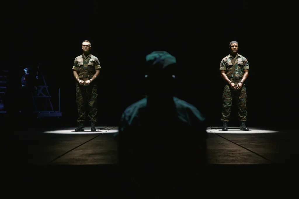 Scene from A Few Good Men featuring two soldiers standing in spotlights, viewed past a silhouetted figure in the foreground.
