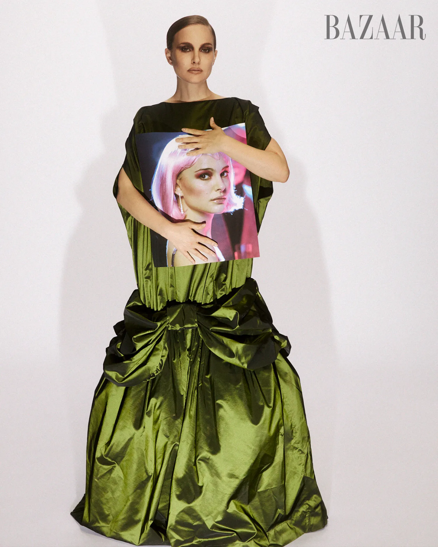 Natalie Portman wearing a green gown and holding a framed picture of herself with pink hair.