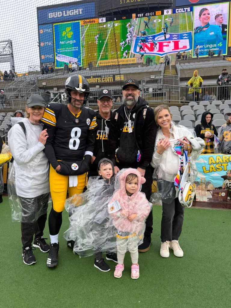 Aaron Rodgers and his family pose for a photo on a football field.