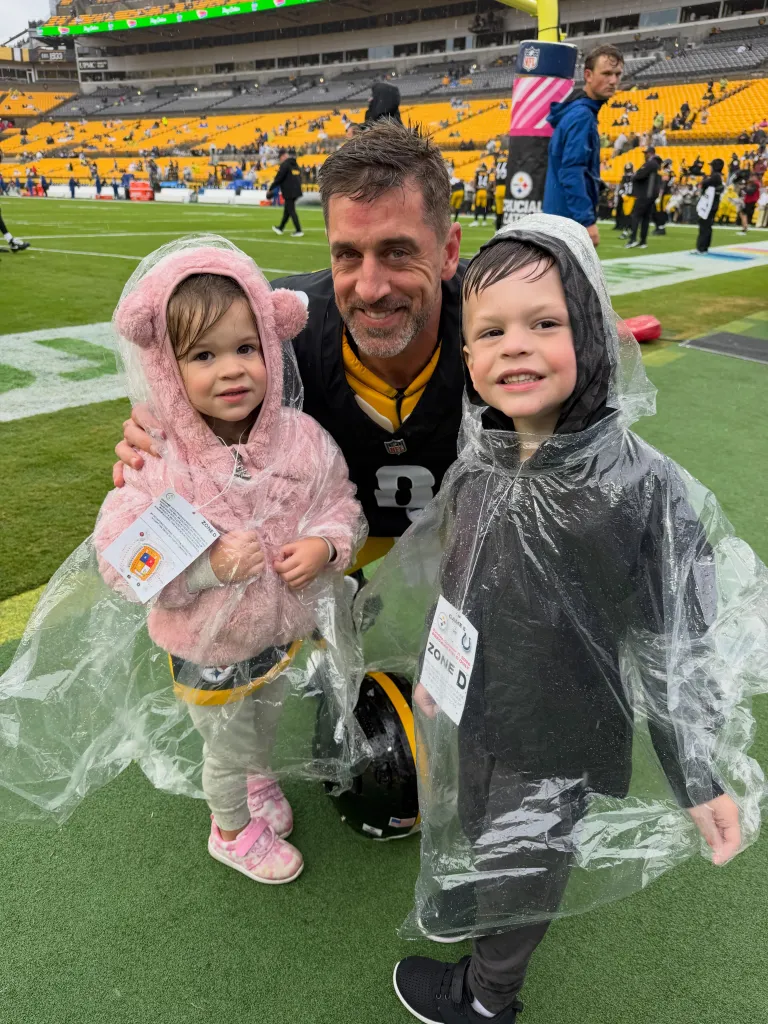 Aaron Rodgers posing with two young children on a football field.