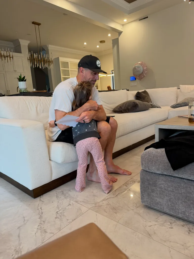 Luke Rodgers hugs a young family member in a living room.