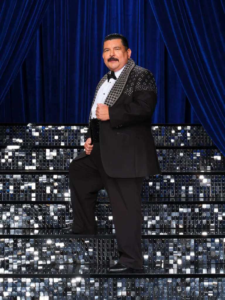 Guillermo Rodriguez posing on a sparkling staircase in a black and silver tuxedo.